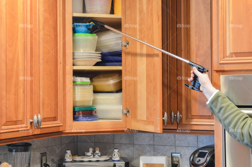 Person using a reacher to assist in getting a bowl from a kitchen cabinet