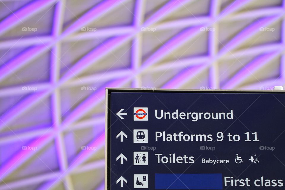 An information sign at London's King's Cross train station with the famous purple, lattice roof in the background.