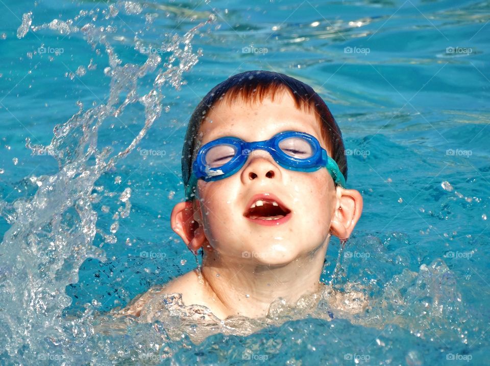 Happy Young Swimmer. Young Boy Splashing In The Pool
