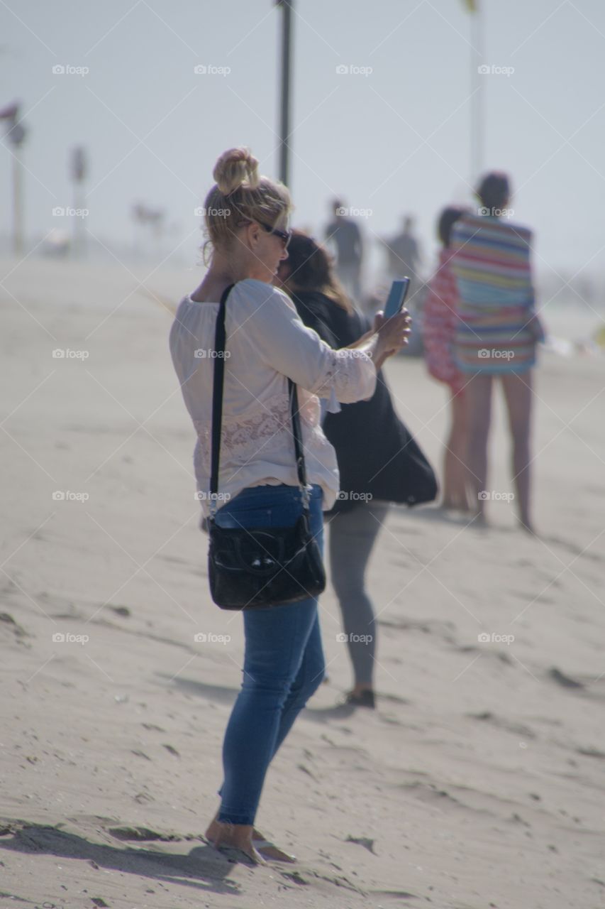 A woman using her phone on the beach to make a photo