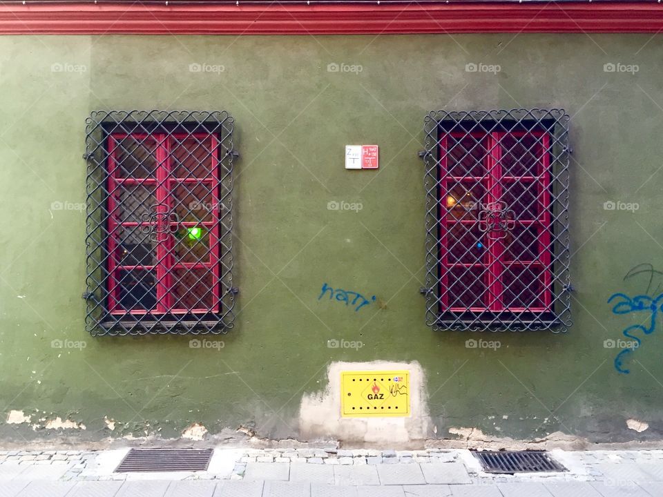 A green wall of a house with fuchsia windows covered with grating