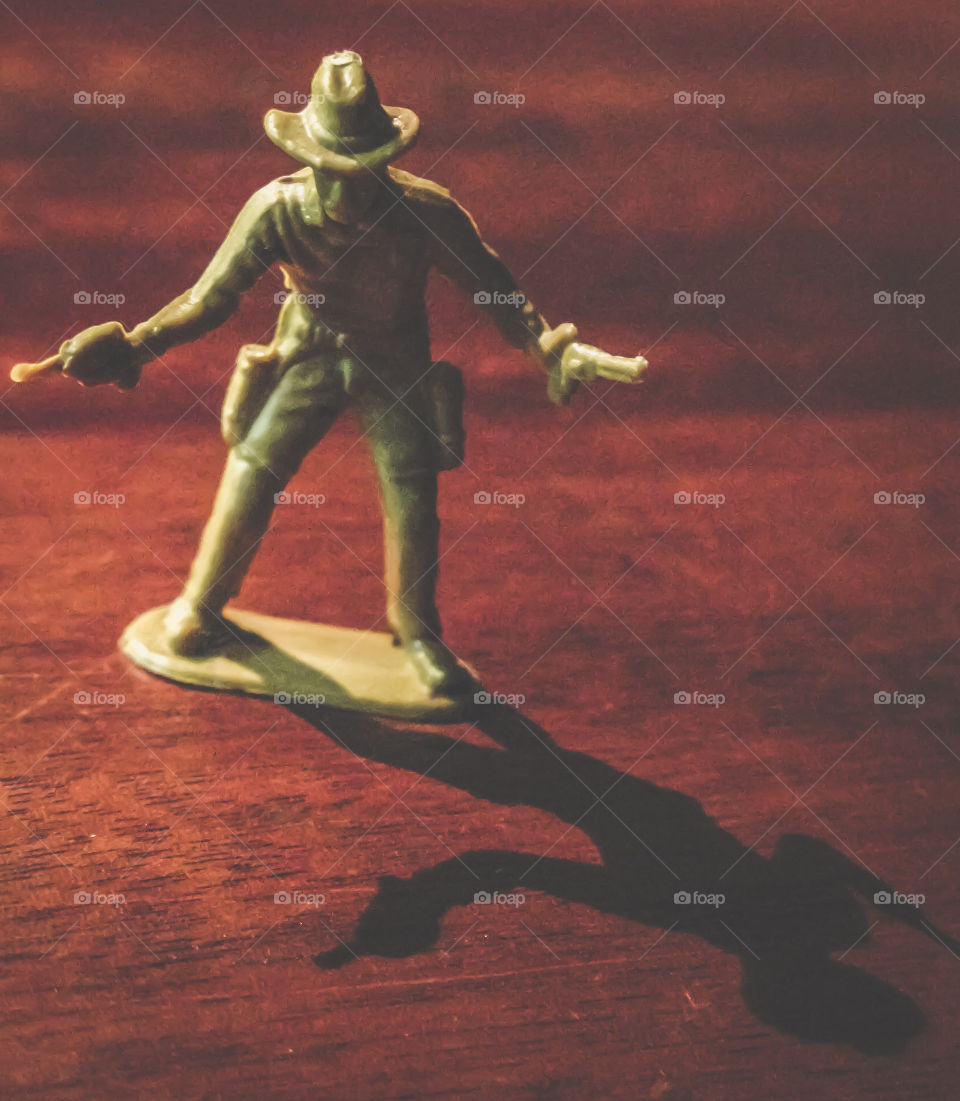 Cowboy action figure casts a long shadow across a wooden surface 