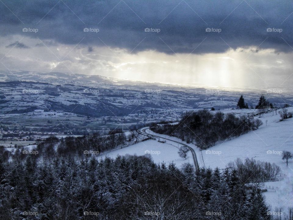 Route de paysage enneigé, forêt et éclaircie à travers les nuages