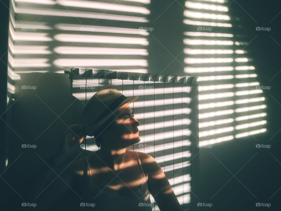 Play of light and shadow.  Portrait of a young woman at home against a background of a white wall with shadows.