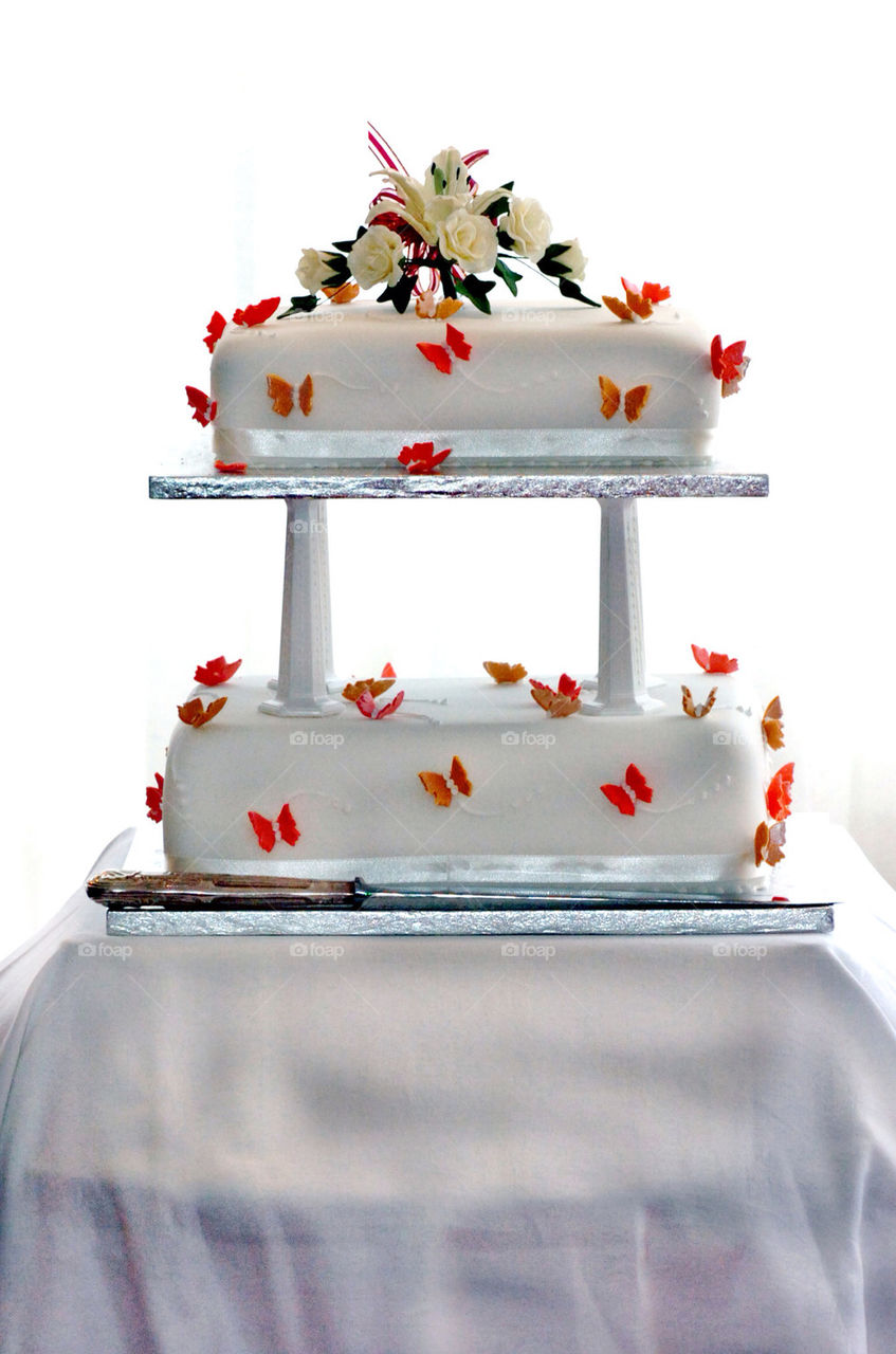 Two tier white wedding cake with white roses on top and tasteful red