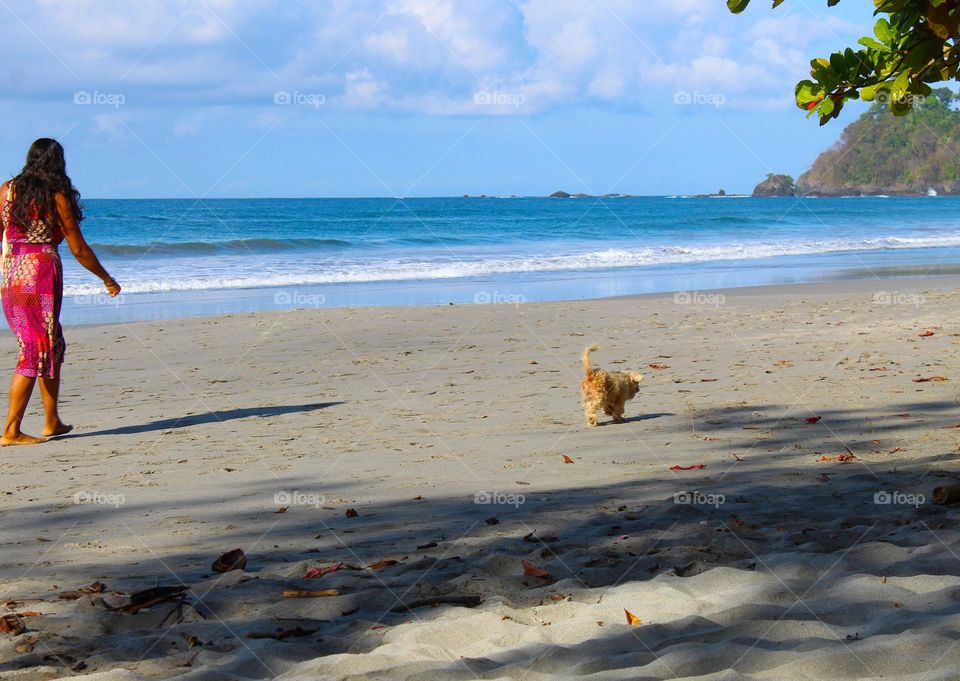 A woman in a red dress walking on the beach with her dog.  Wonderful summer beach landscape of Costa Rica