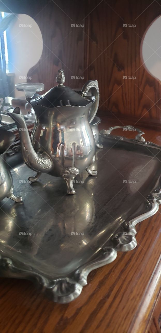 silver tea pot set sits beautifully on a charming china cabinet.