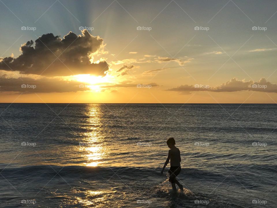 Small boy in the ocean under a golden sunset.
