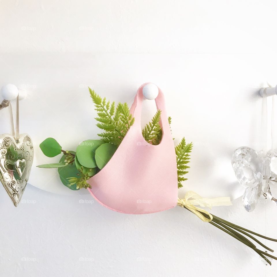 A pink mask holding a bouquet of flowers hanging from a white pegboard.