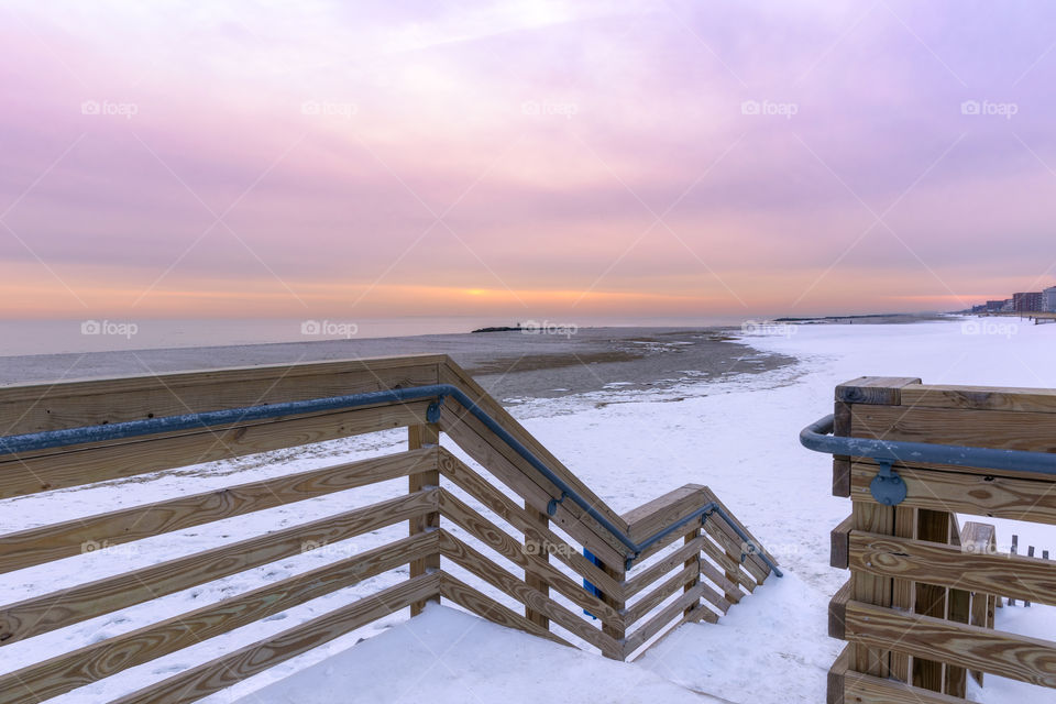 Snow covered boardwalk leading to a wintery December beach seascape, under soft pastel sunset colors