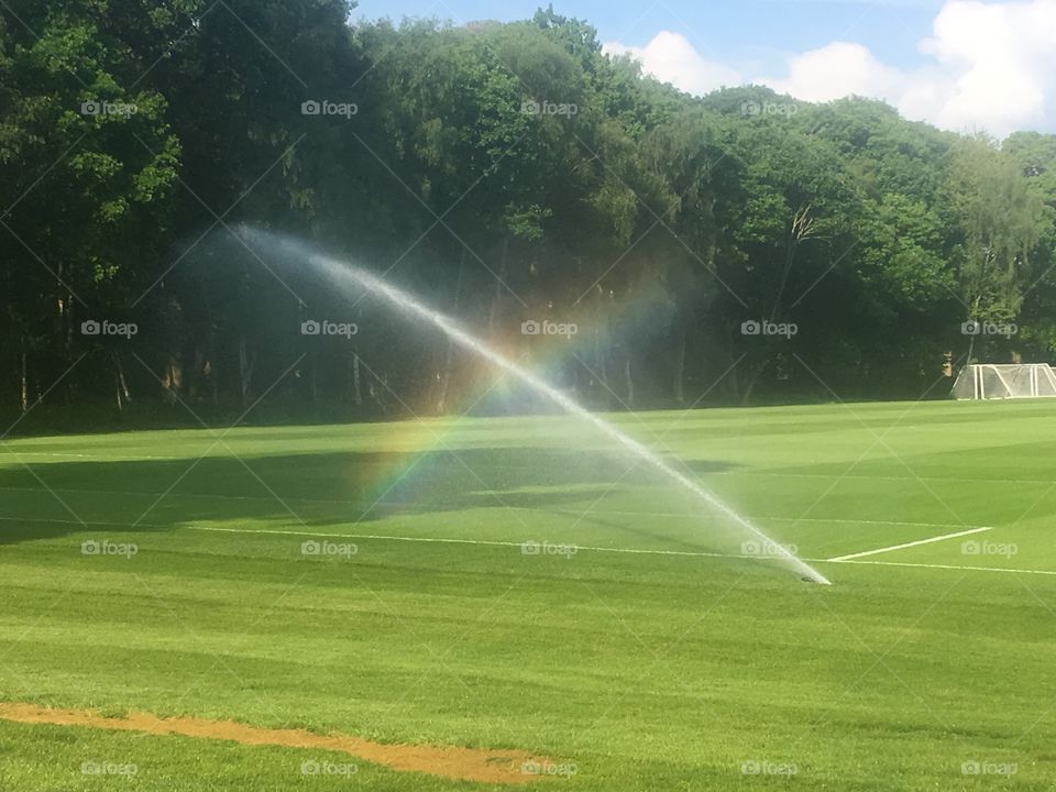Part rainbow across a sprinkler over a football pitch at The Grove Hotel, Watford, Hertfordshire. Spring.