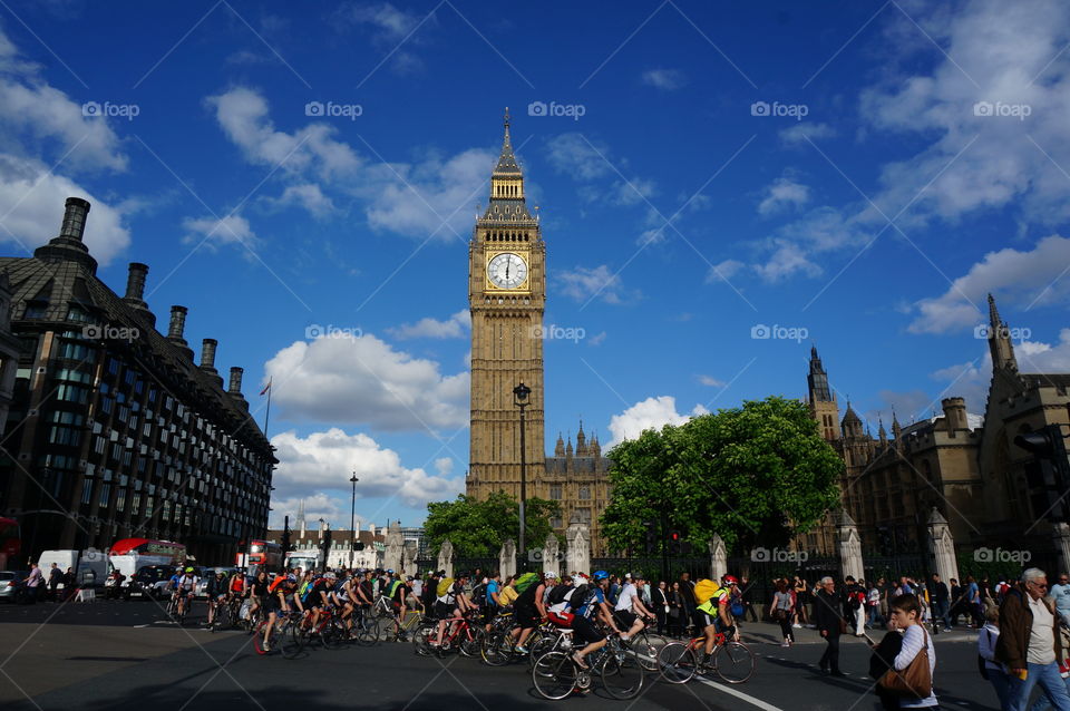 Just some people cycling in front of the big Ben in some great weather while tourists are looking on.