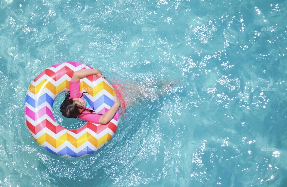 A young girl enjoys floating in a cool blue swimming pool. 