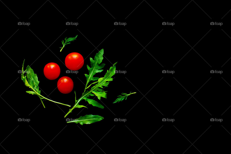 Three cherry tomatoes with ru cola leaves isolated on black