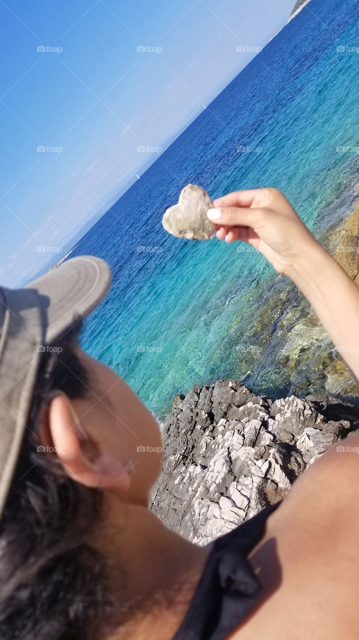 woman holding sculpted rock in the form of a heart. she has a heart of stone. beautiful blue, turquoise, and clear water