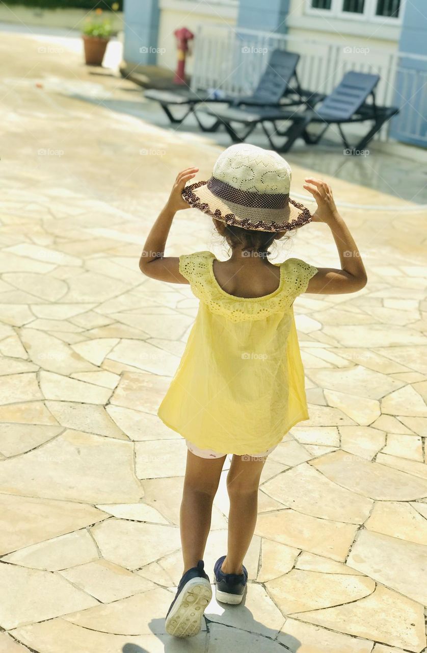 Baby girl in yellow summer outfit and a beautiful cap on her head and holds cap with hands 🙌