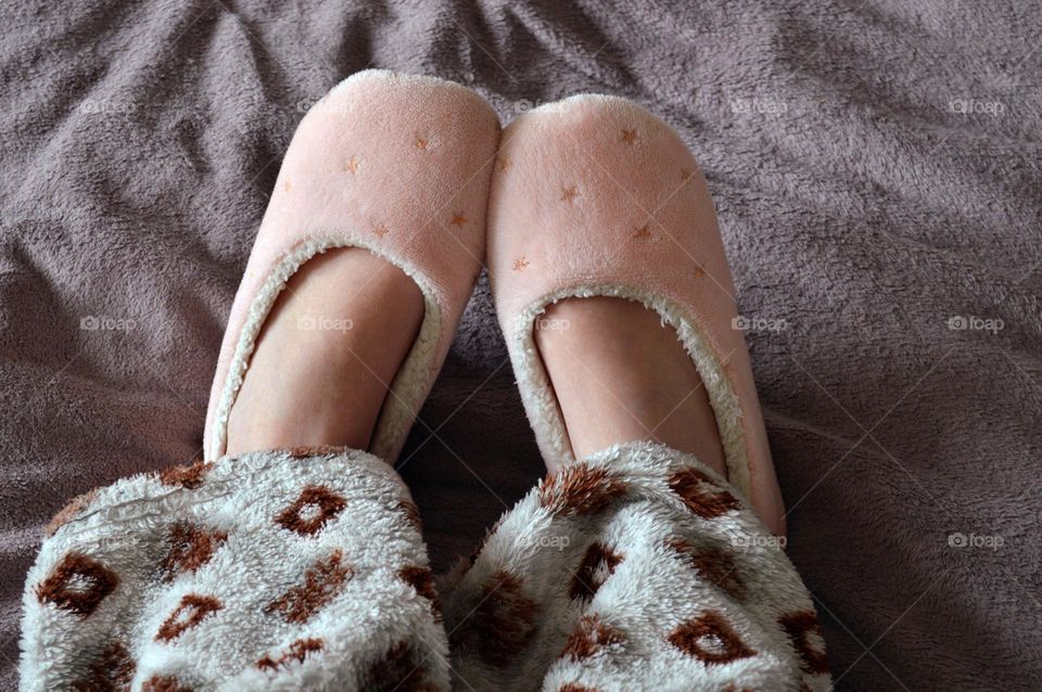 Girl on the bed in warm home slippers and rhombus print pajamas, home comfort and coziness