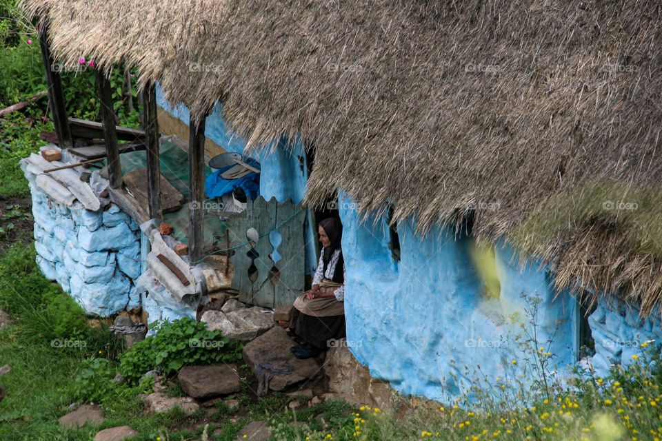 An old woman sitting on the step of her blue house 