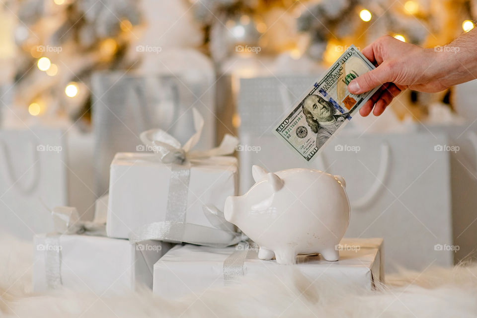 piggy bank with 100 dollars banknote in festive New Year atmosphere of scenery.  Magical bokeh with Christmas tree and bright lights.