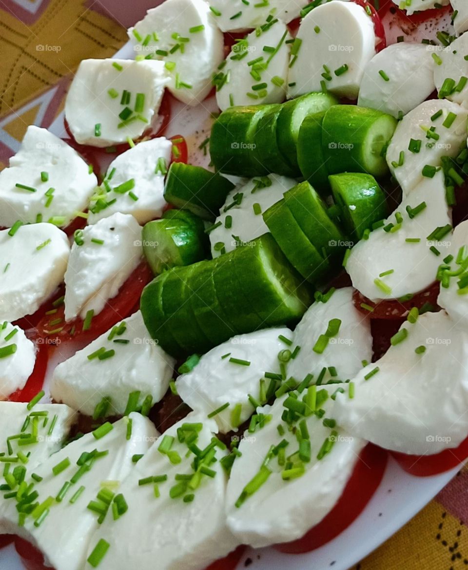 Close up of a plate with tomates, mozzarella, cucumber with a topping of herbs