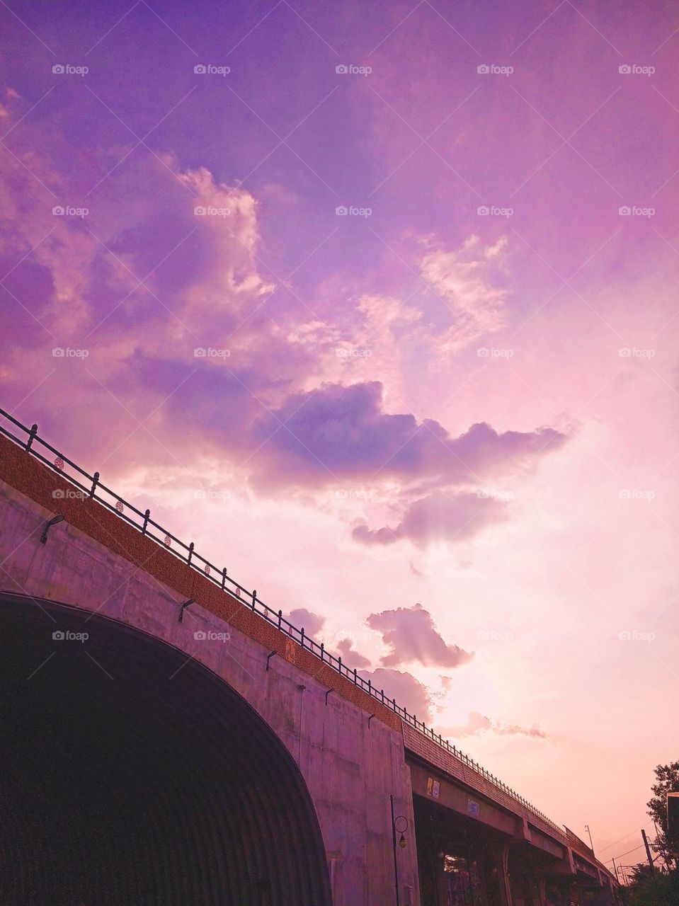 Close-up view of the bridge with a beautiful purple sky and white clouds in the background. A large concrete bridge with a safety fence at the top in low angle view