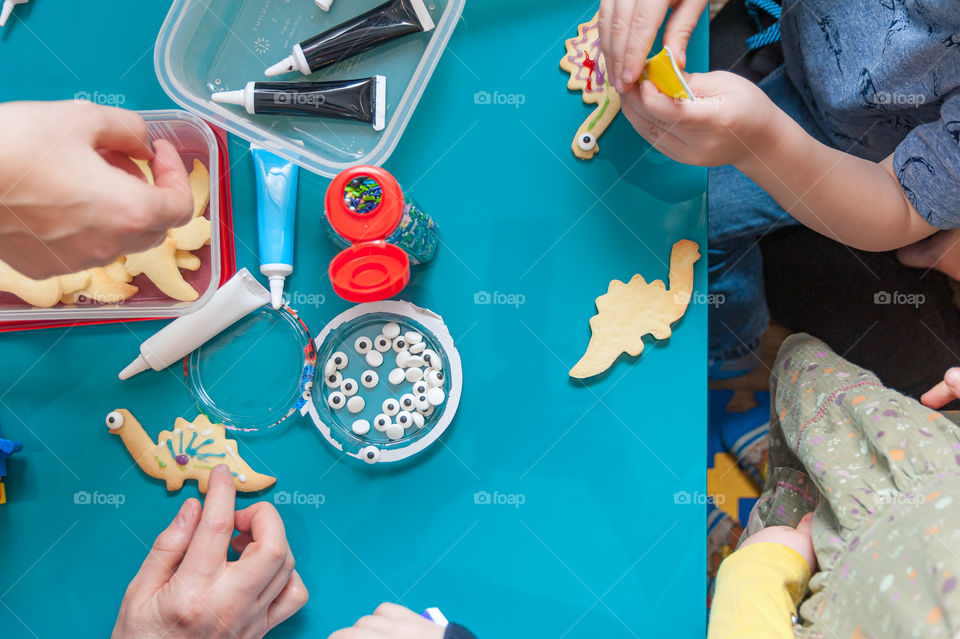 Children with parents having fun decorating home baked dinosaur cookies.