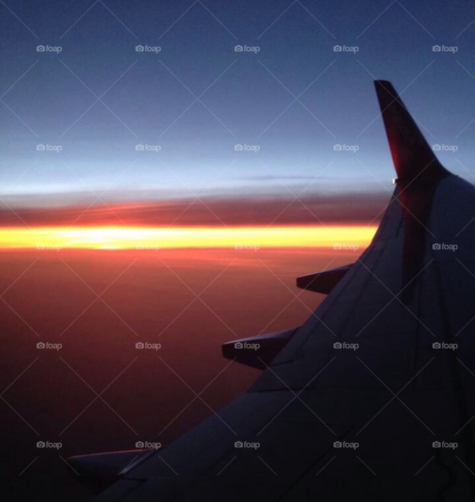 The wing of a commercial airplane flying high above the clouds, paired with a gorgeous sunset.