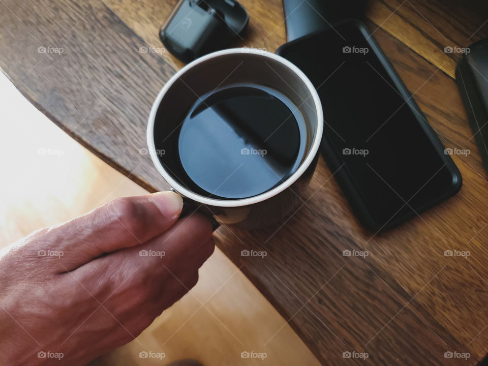 Favorite coffee mug flatlay.  Man placing his favorite coffee mug down on an oak antique wood surface with his cell phone on the right and his wireless ear buds on the left.