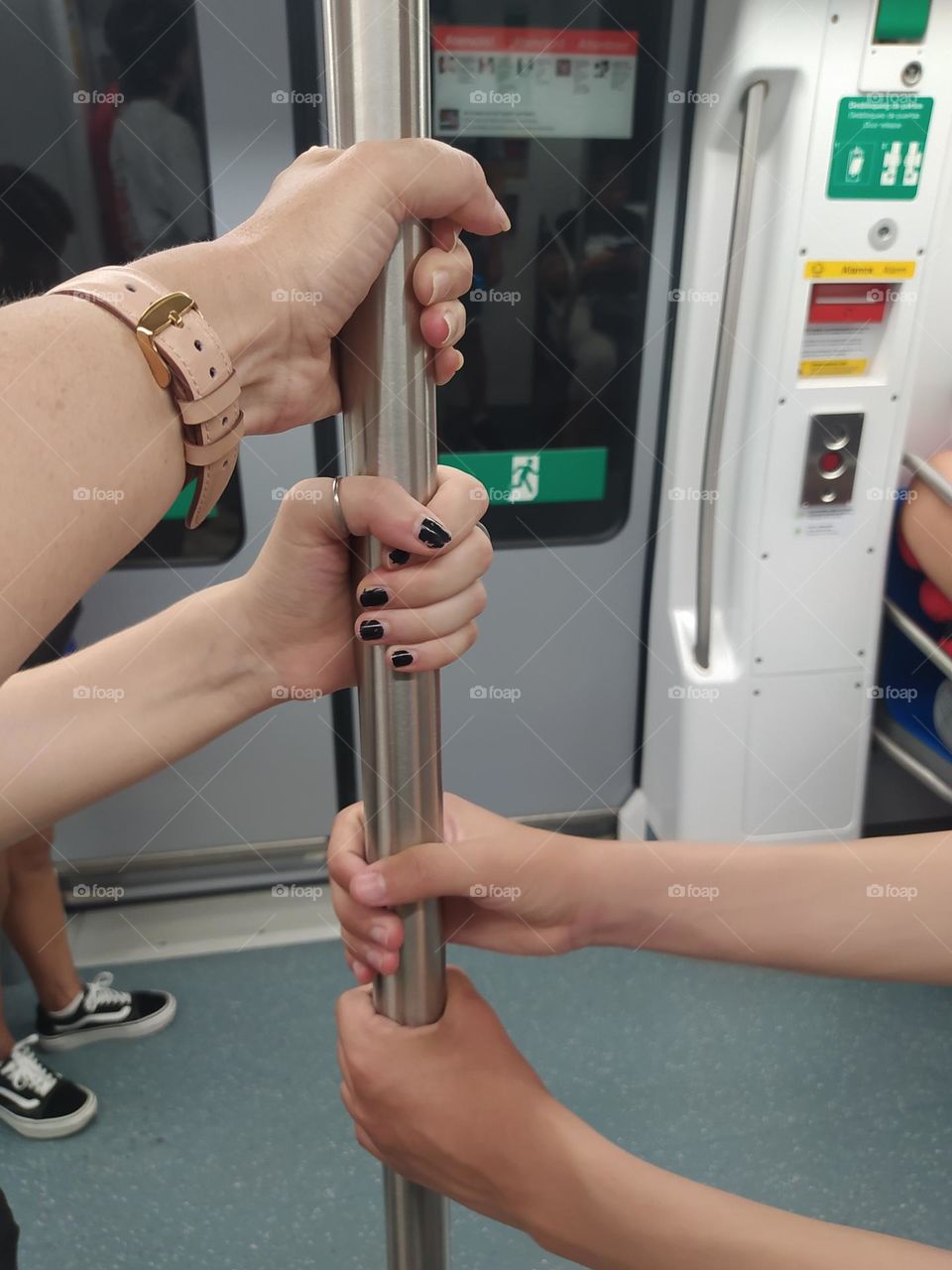 Several different hands hold a bar in the subway. In the background the doors are closed.