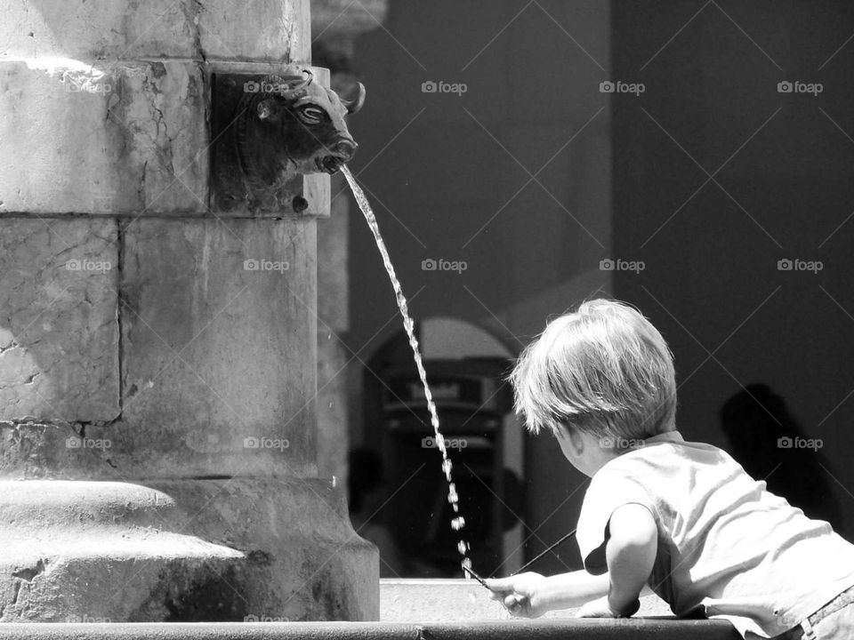 a child plays with the water from an old fountain village. black and white photography highlights simplicity of children's game and nostalgia