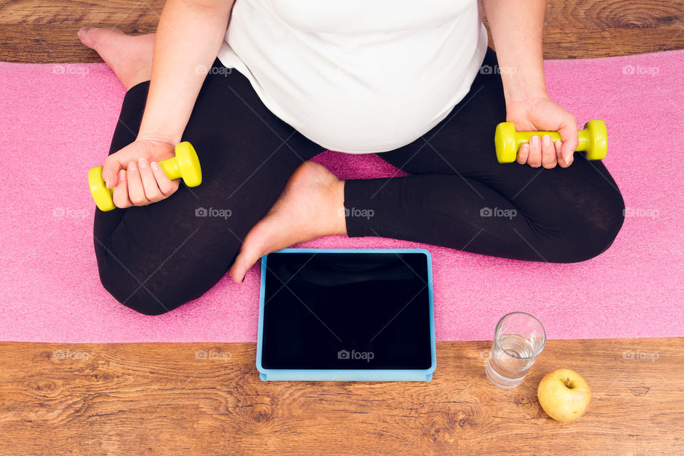 Active pregnant woman with dumbbells exercising with video course