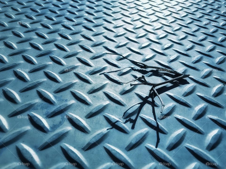 A twig lies on an industrial metallic panel