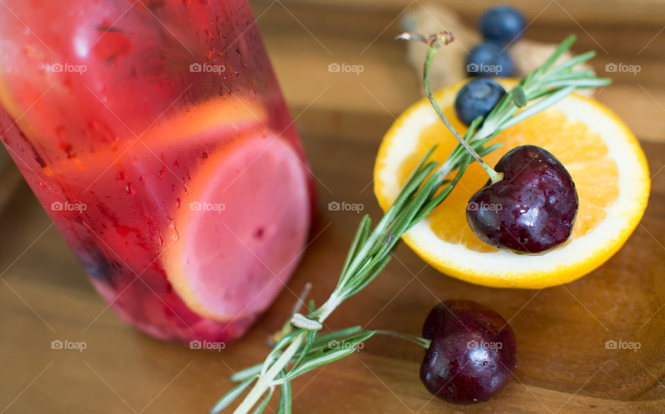 Beautiful summertime detox drink on dark wood with sliced orange, ginger root, blueberry, cherry, and rosemary aromatic herbal flavored water and gourmet juice epicure photography background