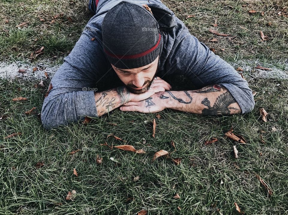 Guy with tattoos laying on his hands in the grass. 