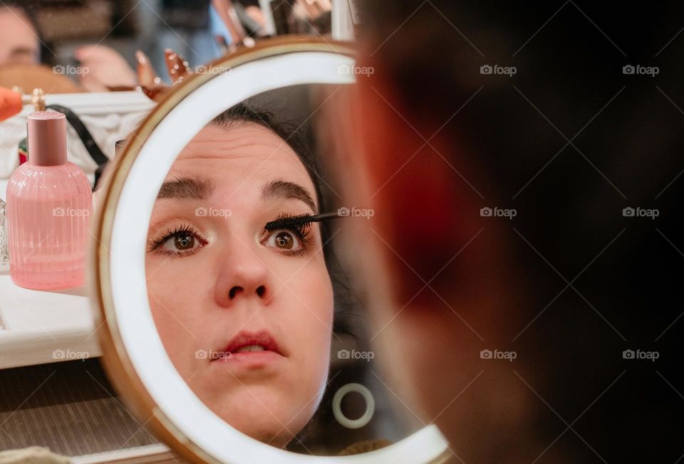 Portrait of young woman doing her make-up in front of circular led illuminated mirror