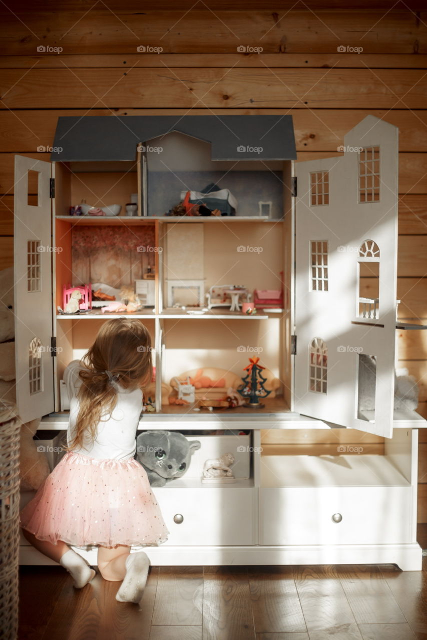 Little girl playing with Dollhouse in playroom 