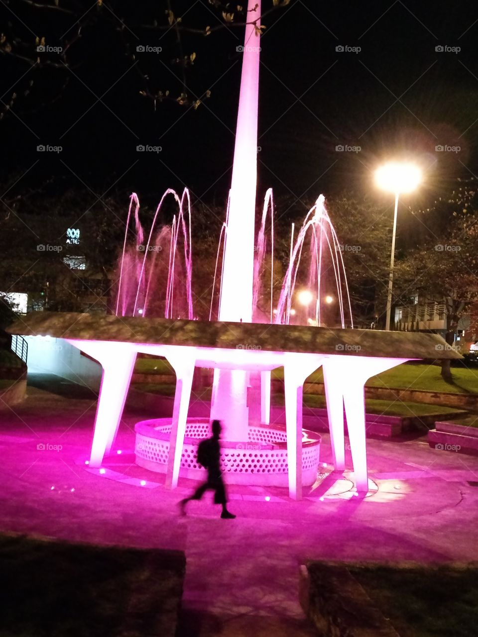 Lone Figure Walking Past illuminated Fountain At Night !