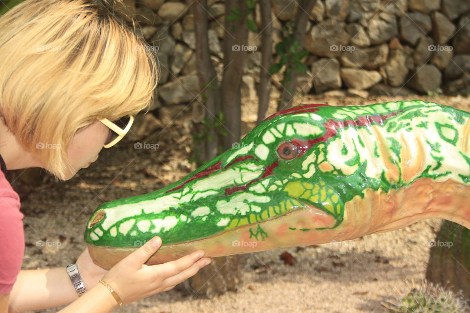 It is a green and brown wooden crocodile. The model is a girl who is giving the crocodile a kiss.