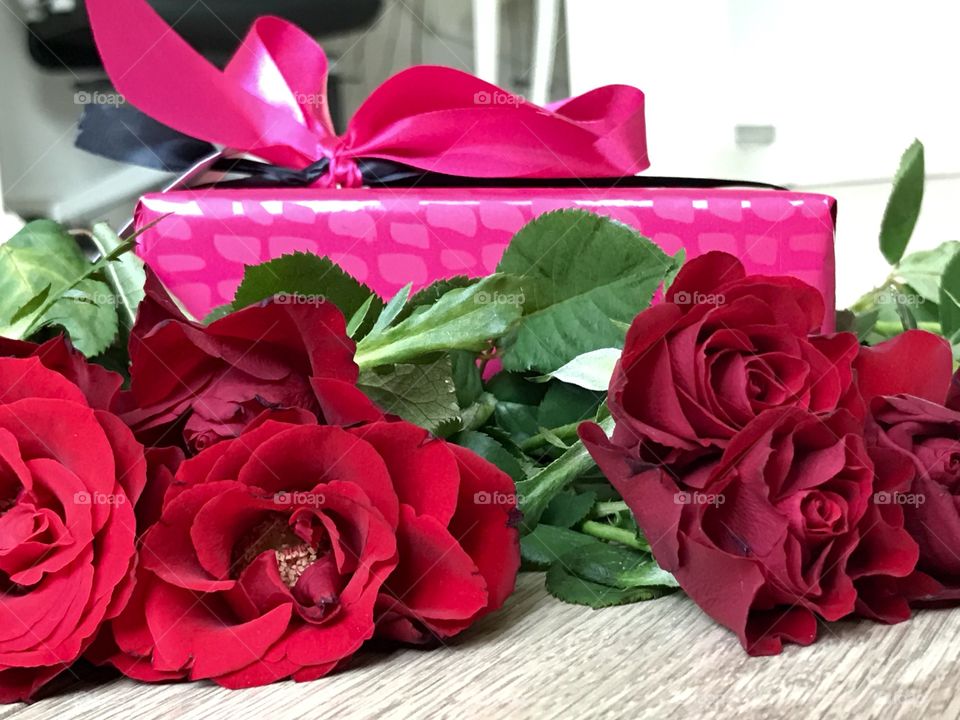 A bouquet of red roses and a pink gift box, wooden background 