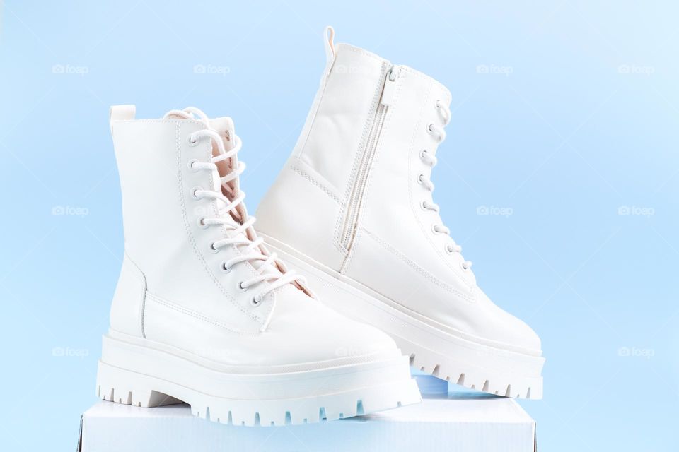 One pair of beautiful white shoes brand Martens standing on a white cardboard box in the center on a light blue background, side view. The concept of fashionable women's shoes.