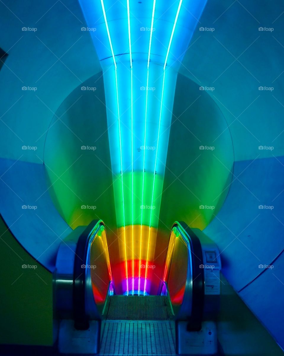 Rainbow fluorescent lights leaning down an escalator at a science center