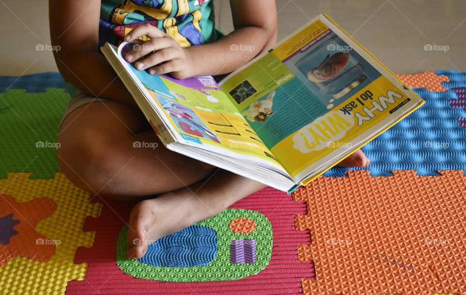 boy reading book sitting on a colorful mat..why do I ask why?