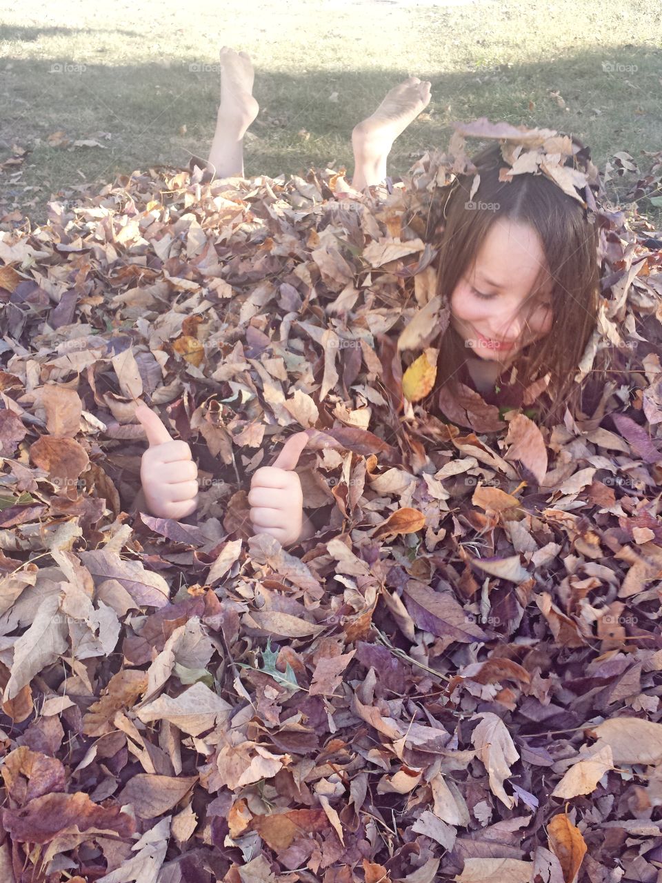 Children covered by dry autumn leaves