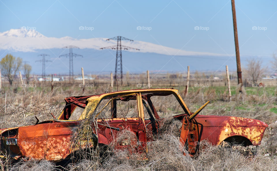 Abandoned and rusty wreckage of an yellow vintage Soviet Russian car in the middle of dry hay with scenic ice top mountains and clear blue sky on the background in rural Southern Armenia in Ararat province on 4 April 2017. 