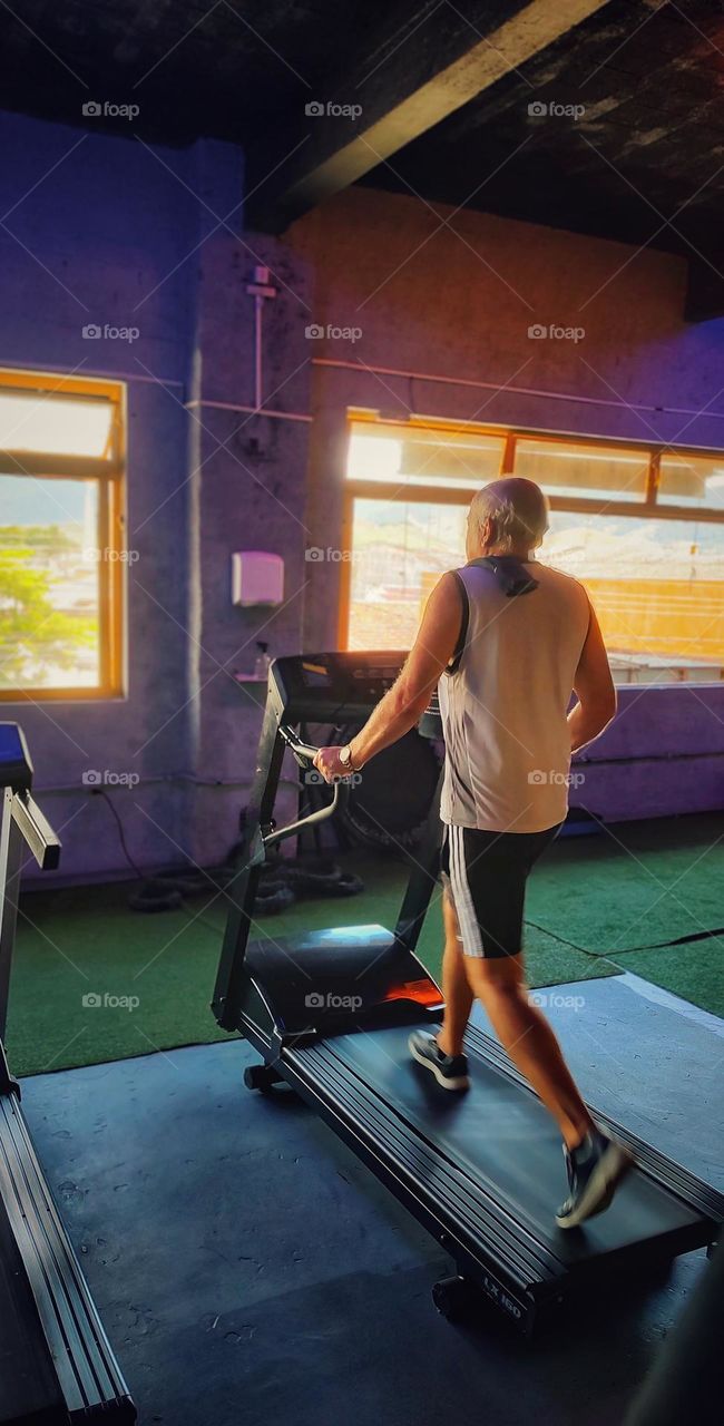 a gentleman in the gym, walking on the treadmill before starting his workout.  Practicing sport is good for the body and soul.