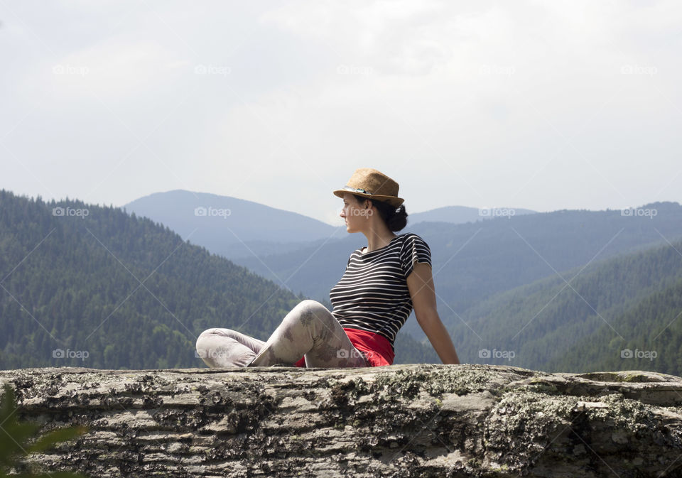 Young woman sitting on rock in the mountain, looking away