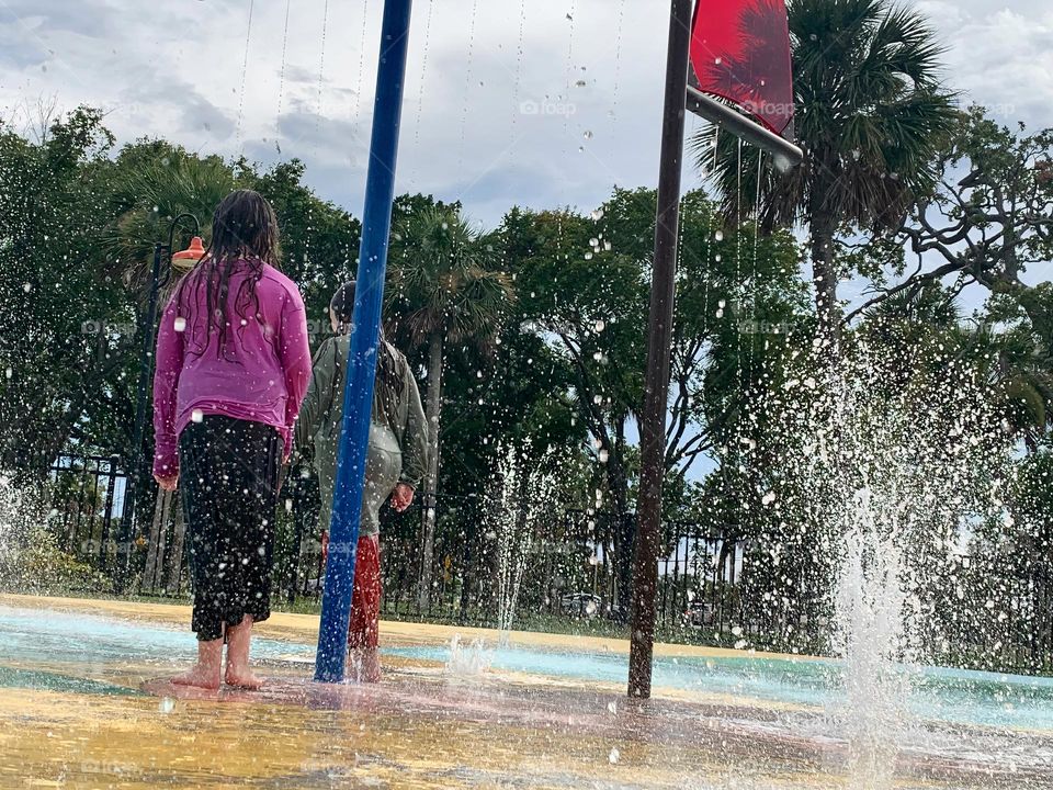 Children having lots of fun in the water at the colorful kids splash pad at the city park for children during a really warm day in Florida.