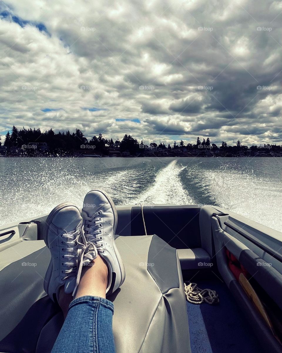 A pair of crisscrossed feet are placed on the inboard motor of a ski boat, cruising on a large lake in summertime 