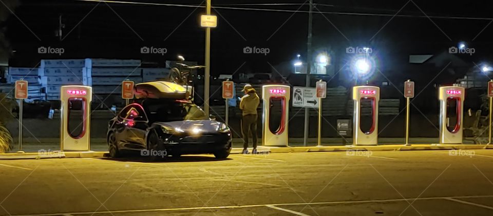 Tesla charging, sailboard and touring bike on roof rack