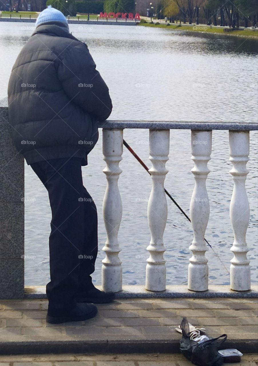 A man stands on the embankment of a pond and catches fish with a fishing rod